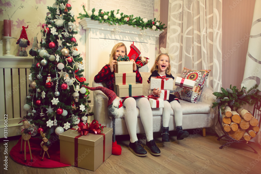 Little girls sitting by the Christmas tree and holding gifts Little girls sitting by the Christmas tree and holding gifts