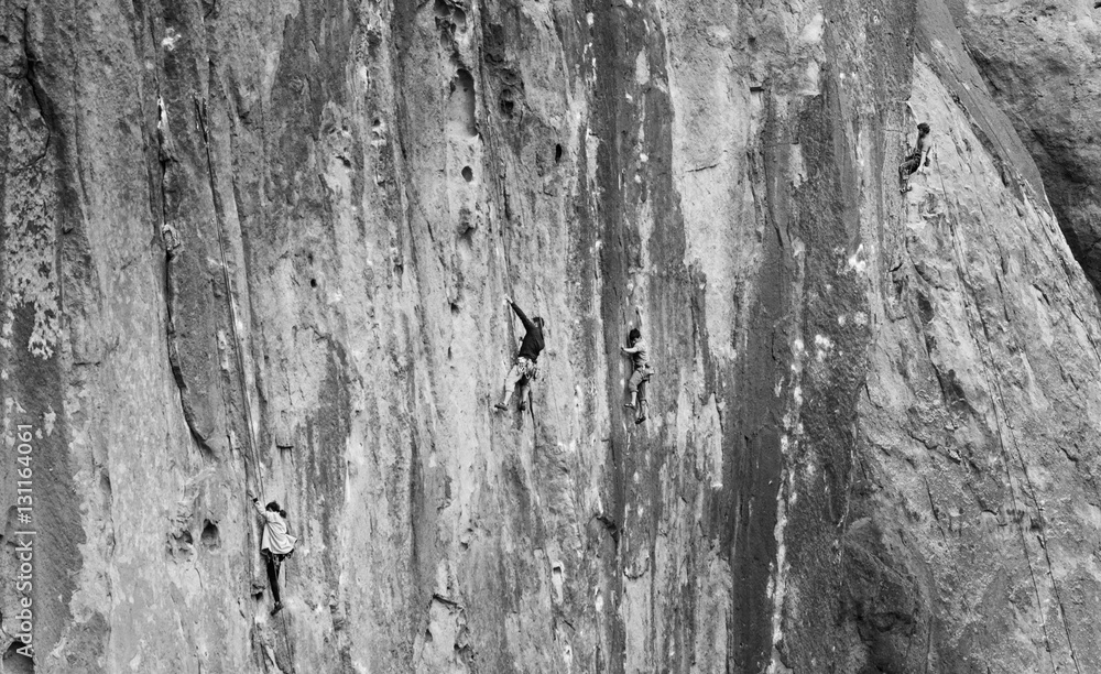 Fototapeta premium Four rock climbers on wall making their way up