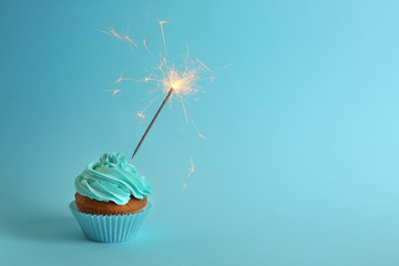 Fresh tasty cupcake with sparkler on blue background