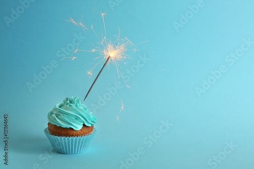 Fresh tasty cupcake with sparkler on blue background