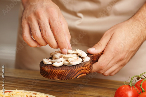 Male hands preparing pizza at wooden table closeup