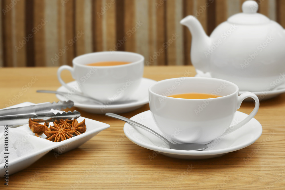 Two cups of tea, tongs and plate with sugar and spices on wooden table Two cups of tea, tongs and plate with sugar and spices on wooden table