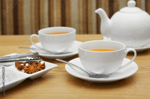 Two cups of tea, tongs and plate with sugar and spices on wooden table