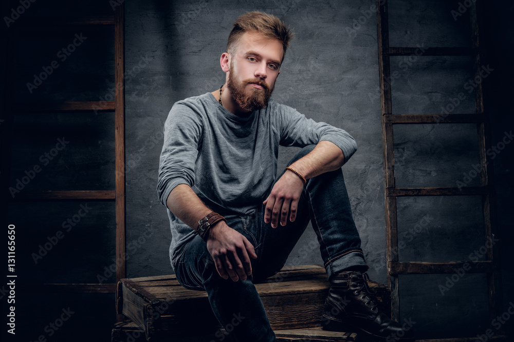 A bearded urban male in a jeans sits on a wooden box