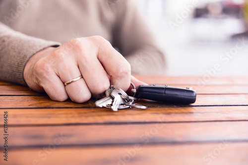 Hands of man holding the car keys with black wallet on wooden table