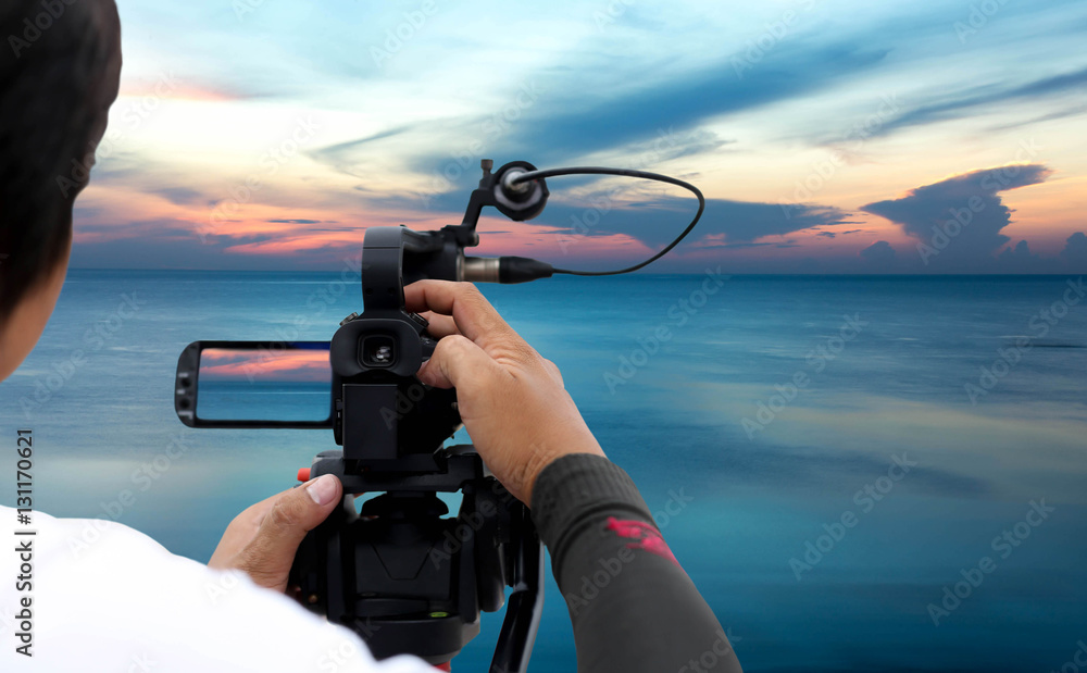 Obraz premium Man recording a sunset on the ocean with video recorder