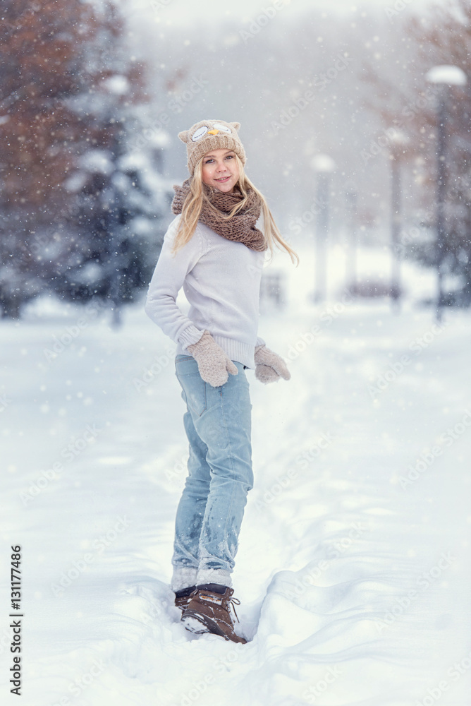Attractive young blonde girl walking in winter forest. Pretty woman in wintertime outdoor. Wearing winter clothes. Knitted sweater, scarf, hat and mittens. Attractive young blonde girl walking in winter forest. Pretty woman in wintertime outdoor. Wearing winter clothes. Knitted sweater, scarf, hat and mittens.