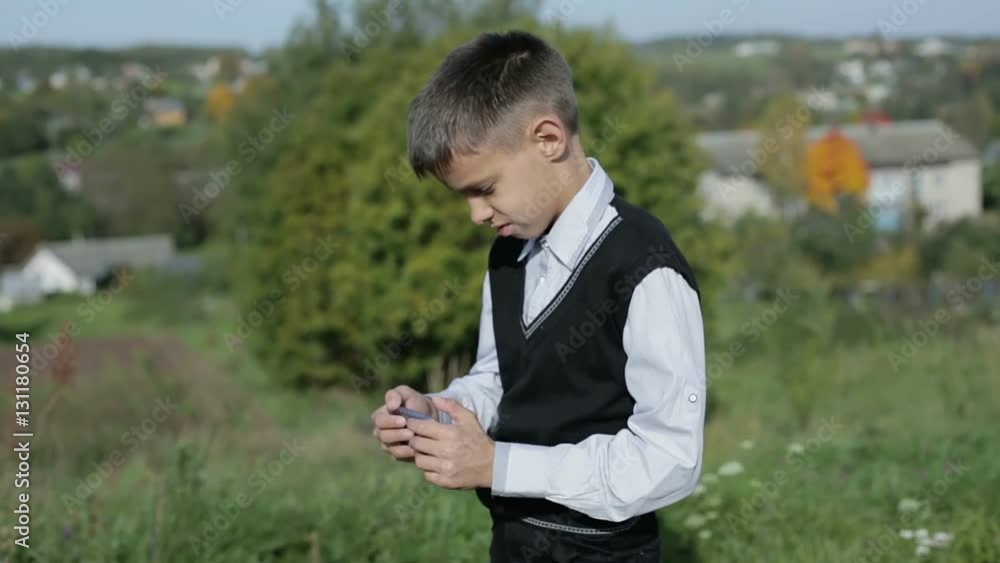 Schoolboy boy is standing outdoors and playing on the mobile phone. Schoolboy boy is standing outdoors and playing on the mobile phone.