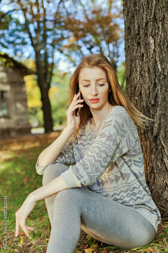 Beautiful girl with long blond hair and blue eyes talking on the phone. Location of autumn park. Beautiful girl with long blond hair and blue eyes talking on the phone. Location of autumn park.