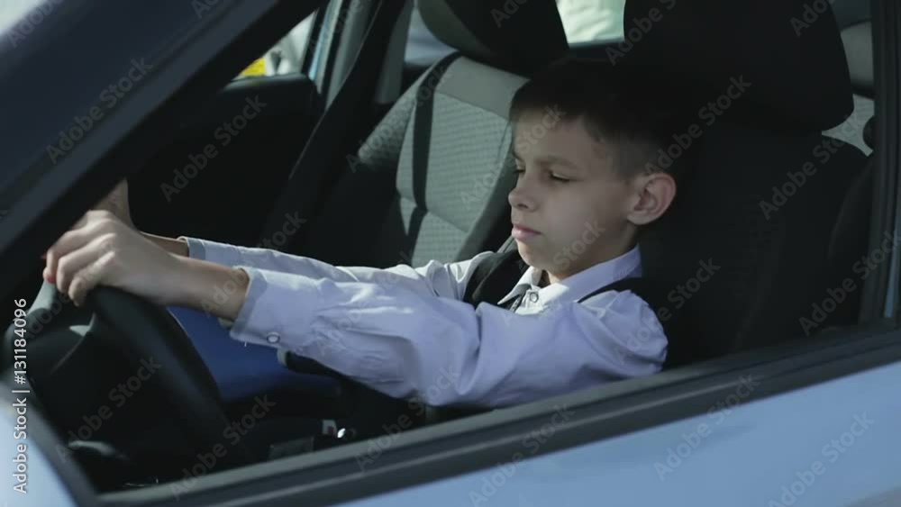 The boy is sitting behind the steering wheel of the car and dreams to drive like an adult. The boy is sitting behind the steering wheel of the car and dreams to drive like an adult.