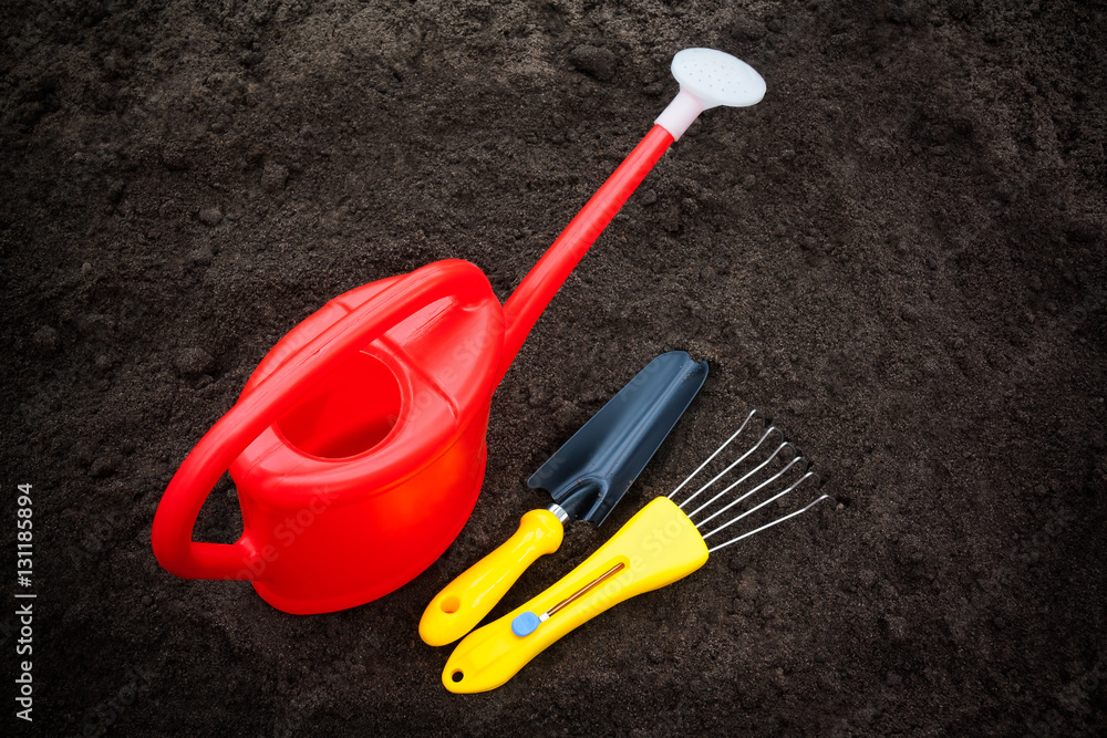 Red watering can, rake and shovel on soil Red watering can, rake and shovel on soil