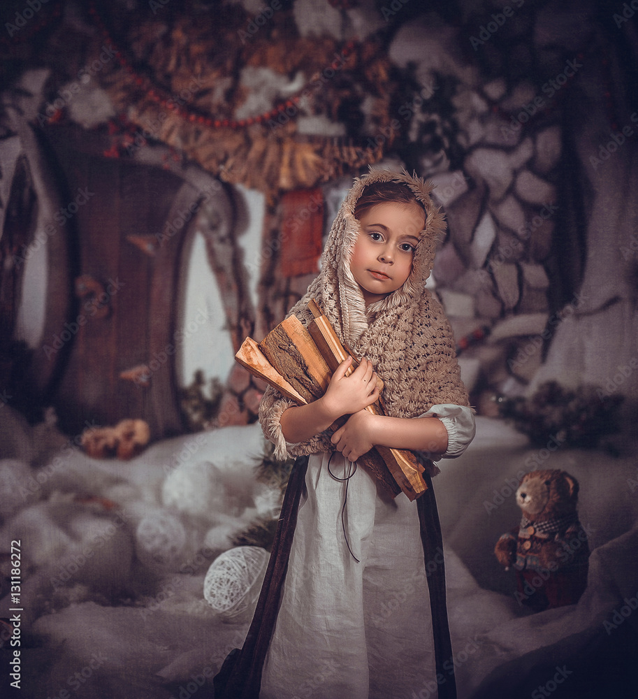 Child in fairytale image of Cinderella, in a beautiful handkerchief and white apron.  She stands with firewood in his hands and looking at camera.Fantastic decoration.Fashionable toning.Creative color