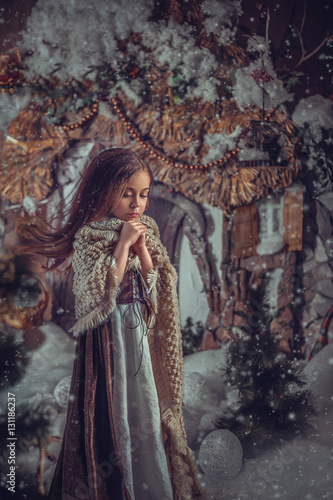 Little girl is wrapped in a beautiful warm shawl, and warming his hands with his breath.Snow, wind develops hair.Shooting in image of Cinderella.Photo high key style.Fashion toning.Creative color.