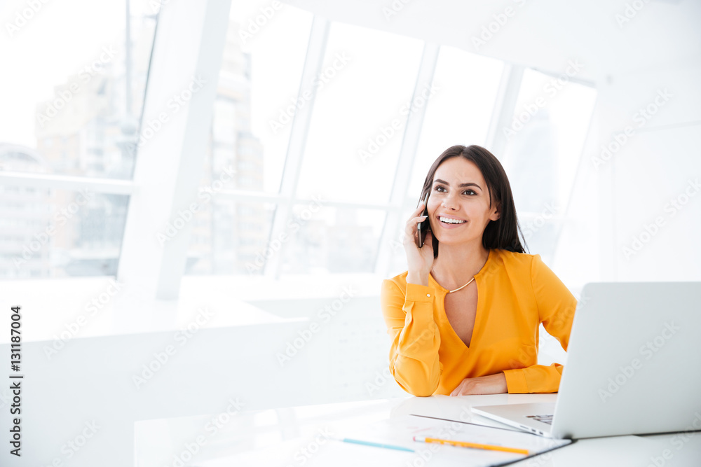 Smiling Business woman talking at phone by the table Smiling Business woman talking at phone by the table