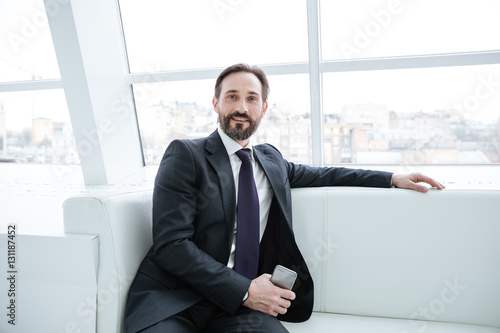 Elderly bearded business man with phone near the window