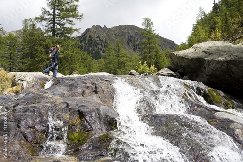 femme avec un sac à dos qui marche sur un rocher au bord d'une cascade 