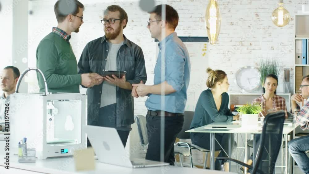 Three Creative Men Discuss Business Matters Passing Tablet Computer to Each Other. People Work in Background. Shot on RED EPIC (uhd). Three Creative Men Discuss Business Matters Passing Tablet Computer to Each Other. People Work in Background. Shot on RED EPIC (uhd).