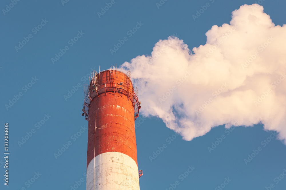 Smoking chimneys against the blue sky / air pollution / steam coming out of the pipe