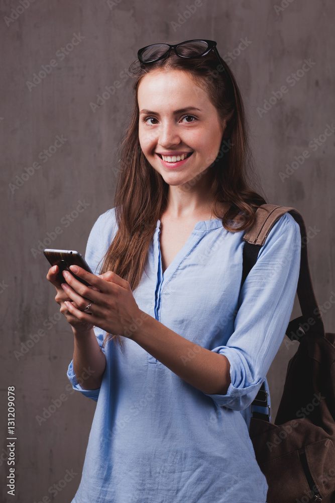 Fototapeta premium Closeup portrait of beautiful happy young woman with glasses chats by cellphone near grey background grunge wall