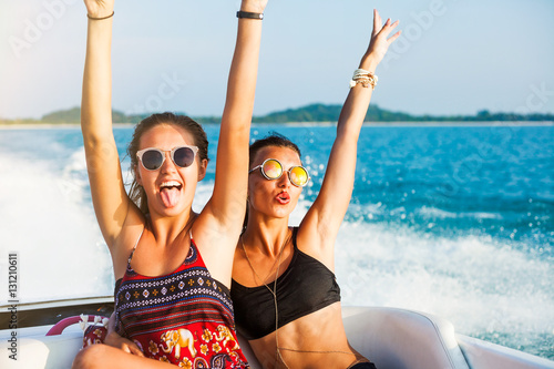 Fototapeta Two beautiful sexy happy hipster girl ride on a speed boat, the girls laugh and