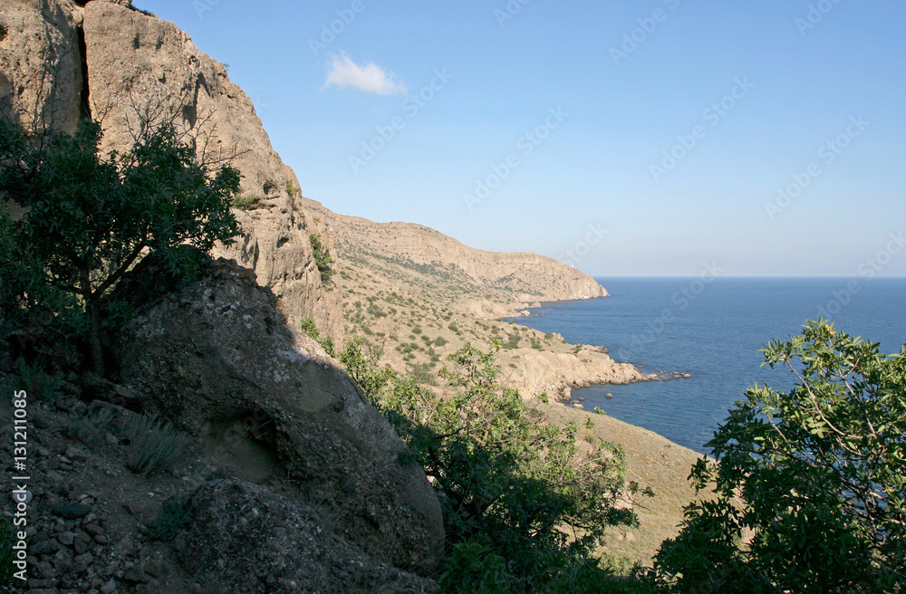 The shore of Black sea with hills, rocks, stones, shrub on the summer sunny day. This photo was taken on the Meganom cape in Crimea. 