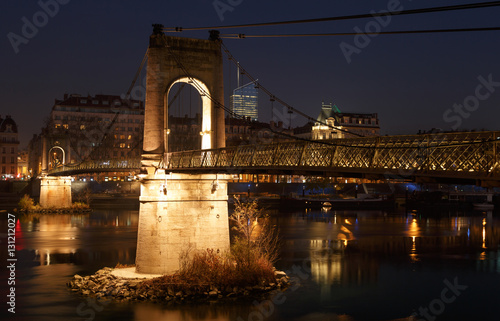 Illuminated Passerelle du College footbridge over the Rhone river in Lyon, France, on a clear evening.
