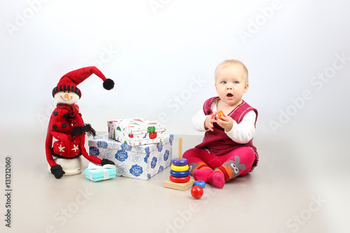 Christmas, X-mas, Holidays, Children concept. Studio shot of adorable sitting baby girl in red dress opening Christmas presents.