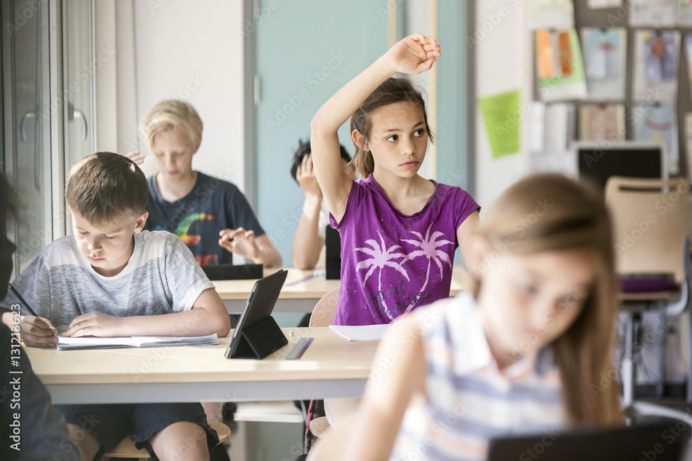 Schoolgirl raising hand at desk in classroom Schoolgirl raising hand at desk in classroom