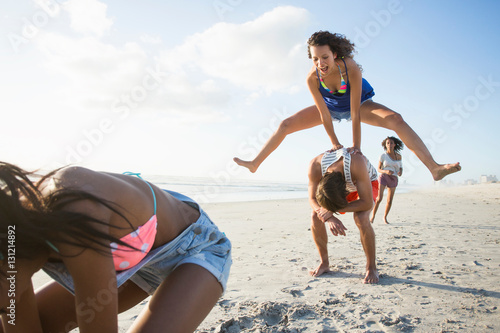 Young man and three female friends playing leapfrog on beach, Cape Town, South Africa