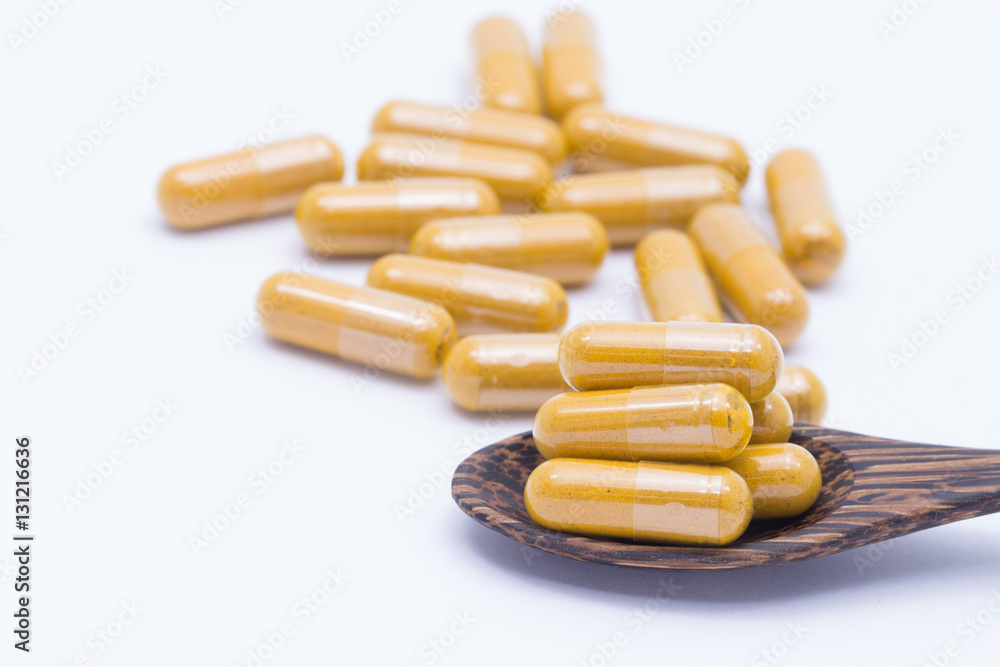 Turmeric powder and a wooden spoon with herbal capsule on white Turmeric powder and a wooden spoon with herbal capsule on white