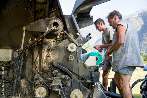 Two male farmworkers untangling netting in hay baler
