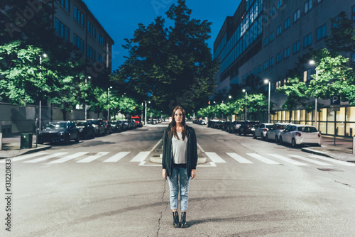 Portrait of young woman standing in centre of city road at night photo