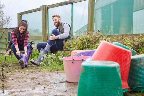 Young couple on farmland putting on rubber boots