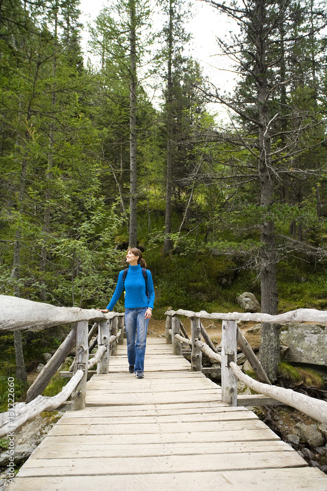 femme souriant qui marche sur un pont en bois dans la forêt avec un sac à dos