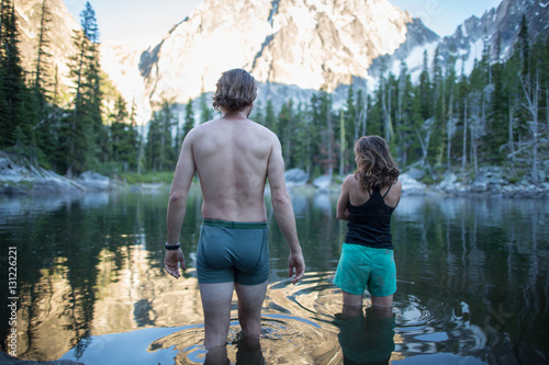 Young man and woman standing in lake, rear view, The Enchantments, Alpine Lakes Wilderness, Washington, USA