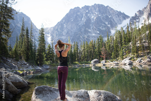 Young woman standing on rock beside lake, looking at view, The Enchantments, Alpine Lakes Wilderness, Washington, USA