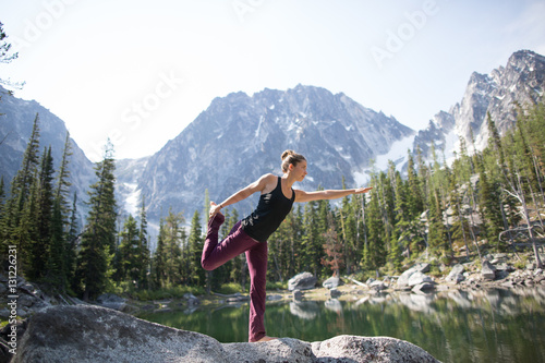 Young woman standing on rock beside lake, in yoga pose, The Enchantments, Alpine Lakes Wilderness, Washington, USA