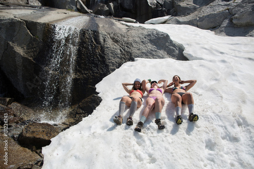 Three young women wearing bikinis, lying in snow, The Enchantments, Alpine Lakes Wilderness, Washington, USA