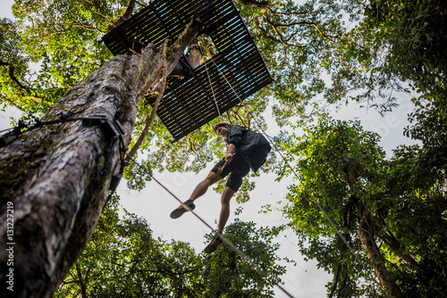 Man hanging from zip line platform in tree, Ban Nongluang, Champassak province, Paksong, Laos photo