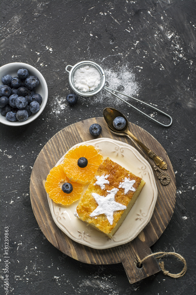 Two servings of homemade juicy mandarin biscuit with asterisks from icing sugar on a dark background. Top view