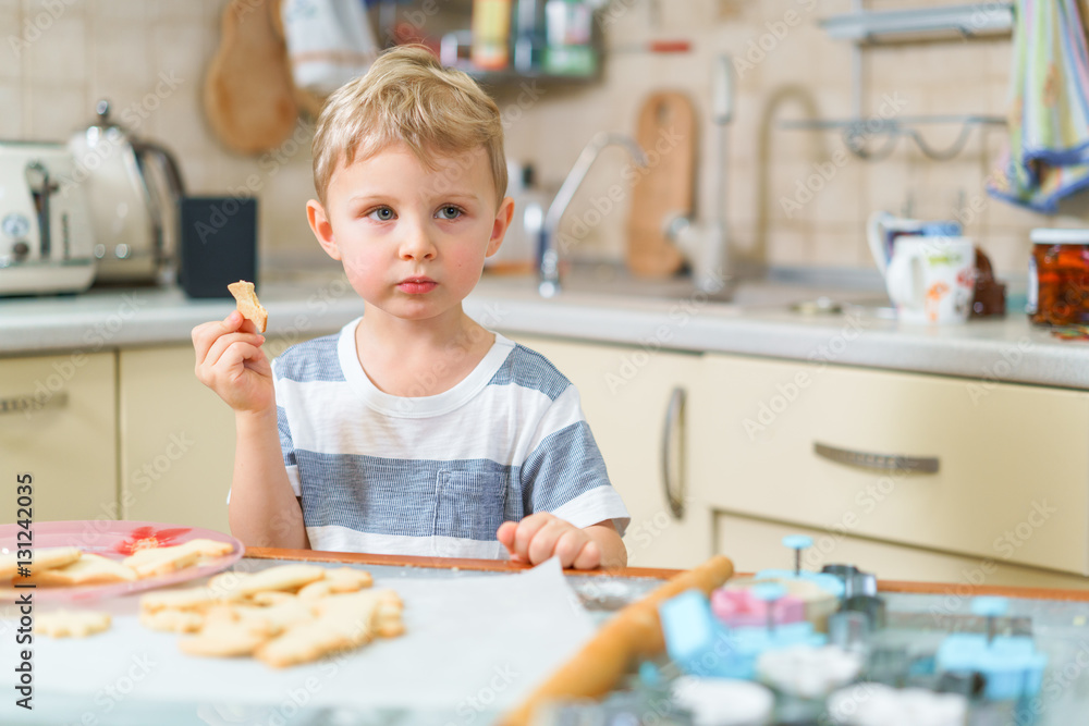 Little blond kid tries freshly baked shortbread, sitting at the kitchen table. Grimacing face. Little blond kid tries freshly baked shortbread, sitting at the kitchen table. Grimacing face.