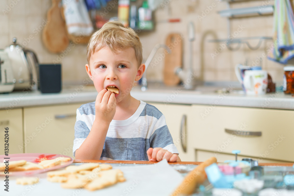 Little blond kid tries freshly baked shortbread, sitting at the kitchen table. Grimacing face. Little blond kid tries freshly baked shortbread, sitting at the kitchen table. Grimacing face.