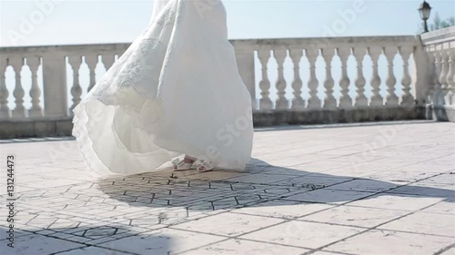 Woman in white dress spinning outdoors no face slow motion low angle. Bride in lace gown dance turning around on terrace balcony floor holding embroidered hem celebrating marriage wedding fashion show
