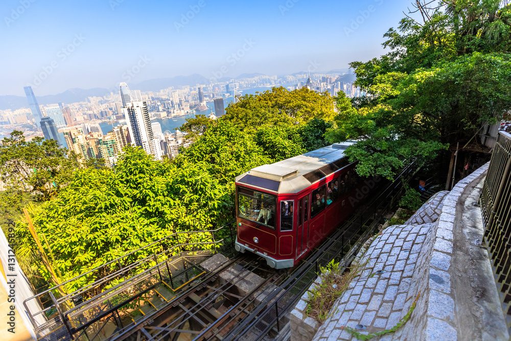 The popular red Peak Tram to Victoria Peak, the highest peak of Hong Kong island. Tourist tram with panoramic city skyline in the background in a sunny day.