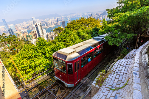 The popular red Peak Tram as he arrives at the terminus of Victoria Peak, the highest peak of Hong Kong island, with panoramic city skyline in background. Sunny day.