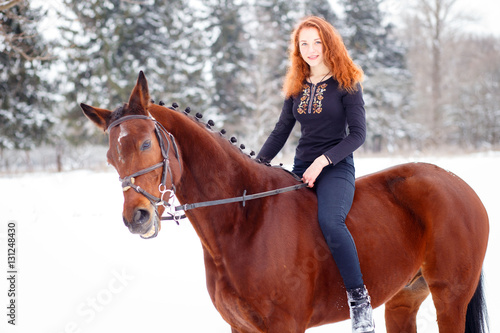Young teenage girl riding bay horse in winter park. Winter horseback riding background