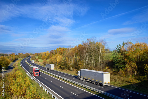 Trucks driving on the asphalt highway in the countryside with trees in autumn colors