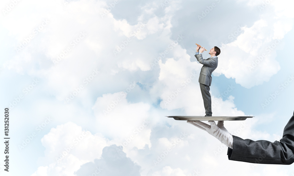Businessman on metal tray playing fife against blue sky background Businessman on metal tray playing fife against blue sky background