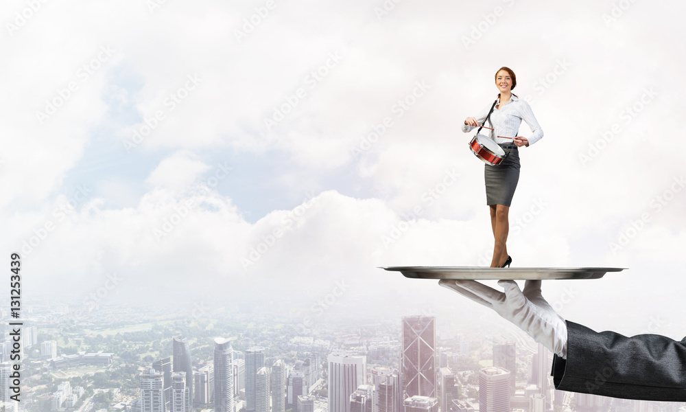 Attractive businesswoman on metal tray playing drums against cityscape background Attractive businesswoman on metal tray playing drums against cityscape background
