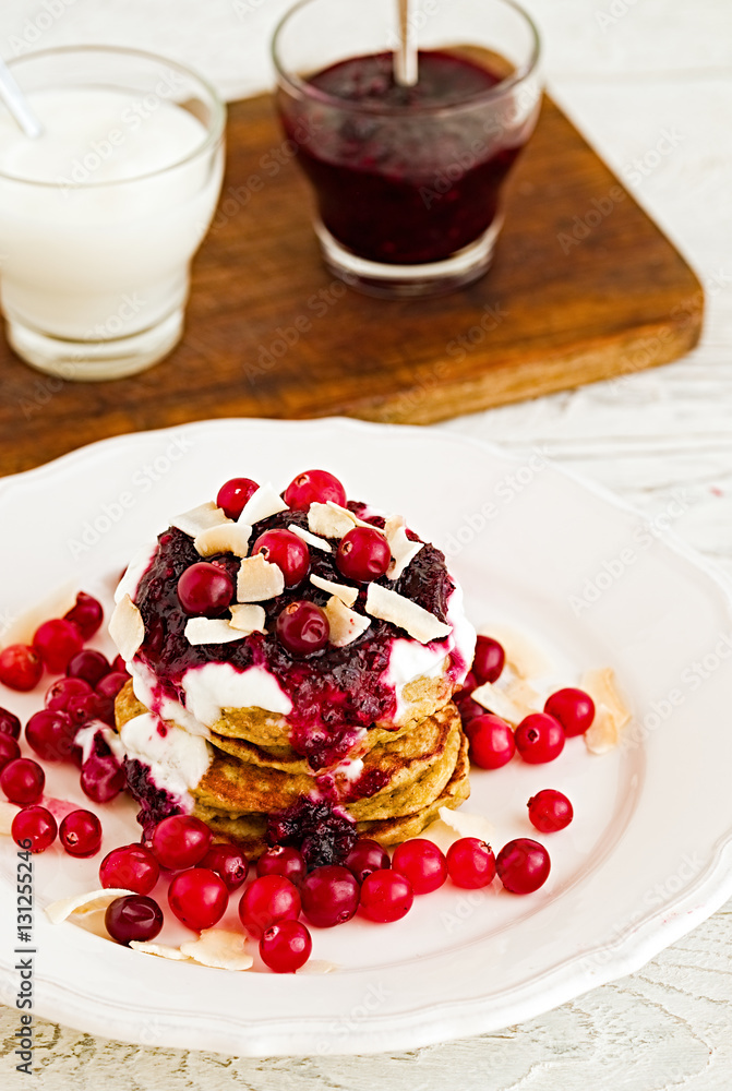 Stack of vegan gluten free pancakes with yogurt, blueberrty jam and canberries on a white plate with red fork and knife. Bright healthy breakfast. White wooden table Stack of vegan gluten free pancakes with yogurt, blueberrty jam and canberries on a white plate with red fork and knife. Bright healthy breakfast. White wooden table